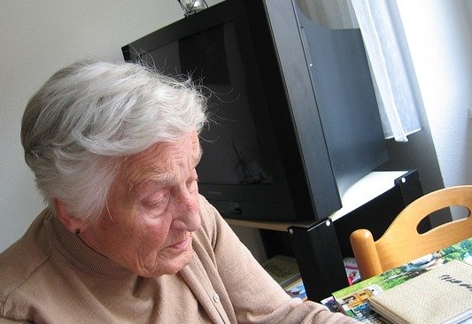 Altere Dame sitzt zu Hause vor einem Fernseher