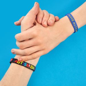 Asperger Autismus Selbsthilfegruppe Ein Arm mit einem Armband am Handgelenk worauf Autismus Tag steht, greift nach einem anderen Arm mit einem Armband worauf Ich habe Autismus steht. Es umschließen sich Ihre Hände.
